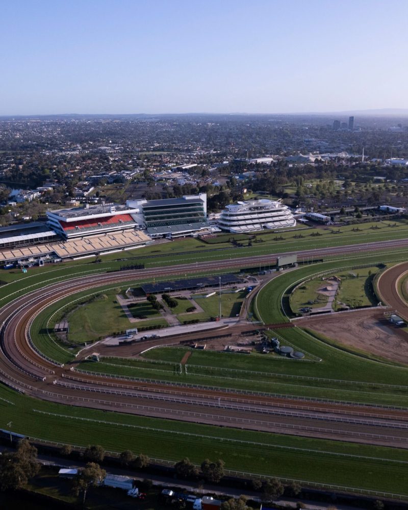 Aerial view of a horse racing track with surrounding cityscape and clear blue sky in the background.