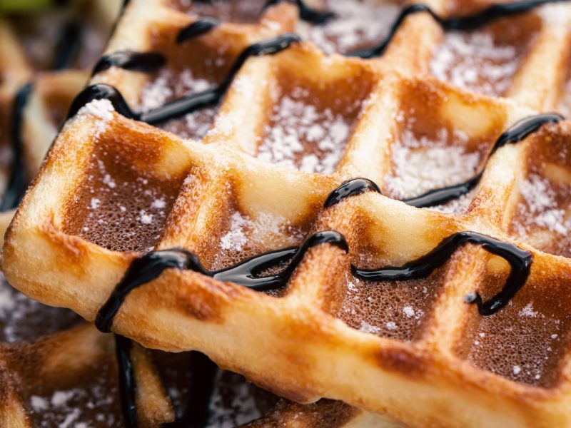 Close-up, appetizing Belgian waffles drizzled with chocolate, soft focus, food background.