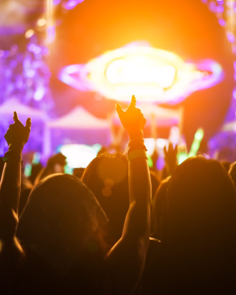 Crowd of hands up concert stage lights and people fan audience silhouette raising hands in the music festival rear view with spotlight glowing effect