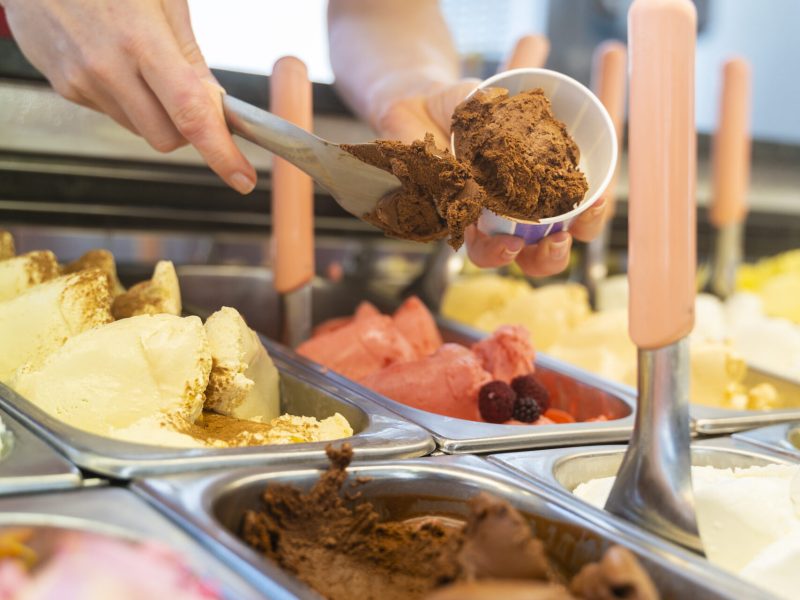 Vertical photo of the interior of an ice cream counter with a saleswoman preparing a chocolate flavored tub