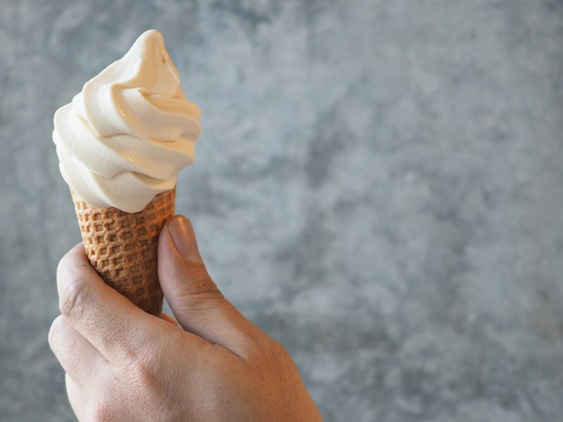 Soft serve ice cream cone in male model's left hand with cement background.